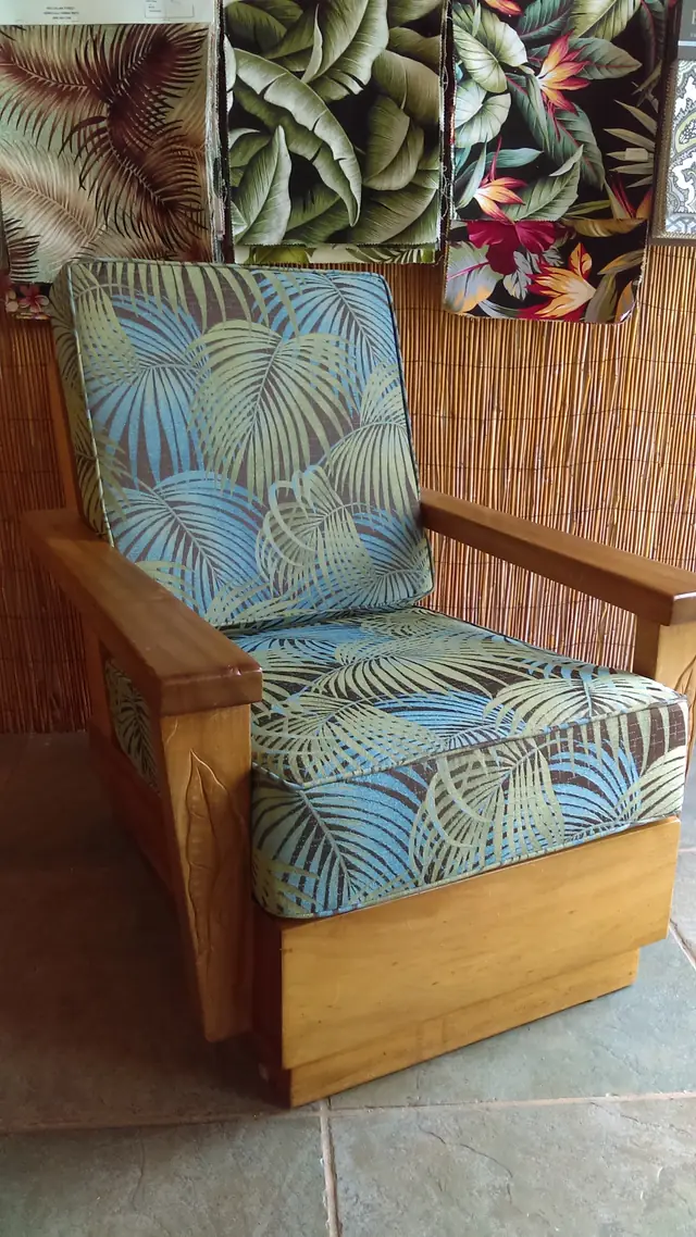 A carved koa-arm lounge chair with new seat and back cushions in blue and green palm-frond fabric