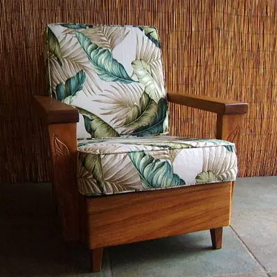 A koa wood chair re-covered in cream palm-leaf fabric against a bamboo wall